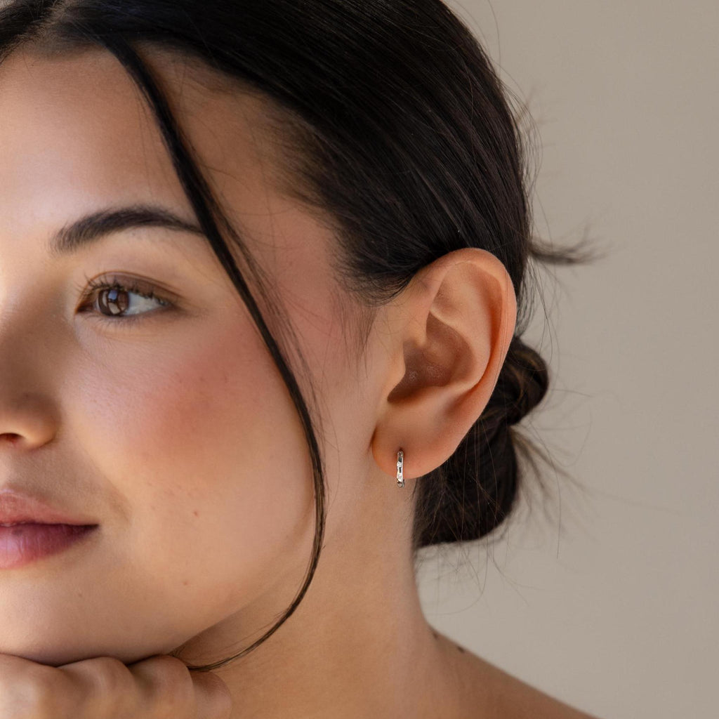 Close-up of a woman with dark hair in a bun, wearing Mini Diamond Sprinkle Huggies, looking to the side.