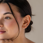Close-up of a woman with dark hair in a bun, wearing Mini Diamond Sprinkle Huggies, looking to the side.