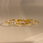 The Trio Diamond Stacking Ring Set, featuring delicate gold bands accented with small diamonds, rests on a smooth, reflective surface bathed in warm light.
