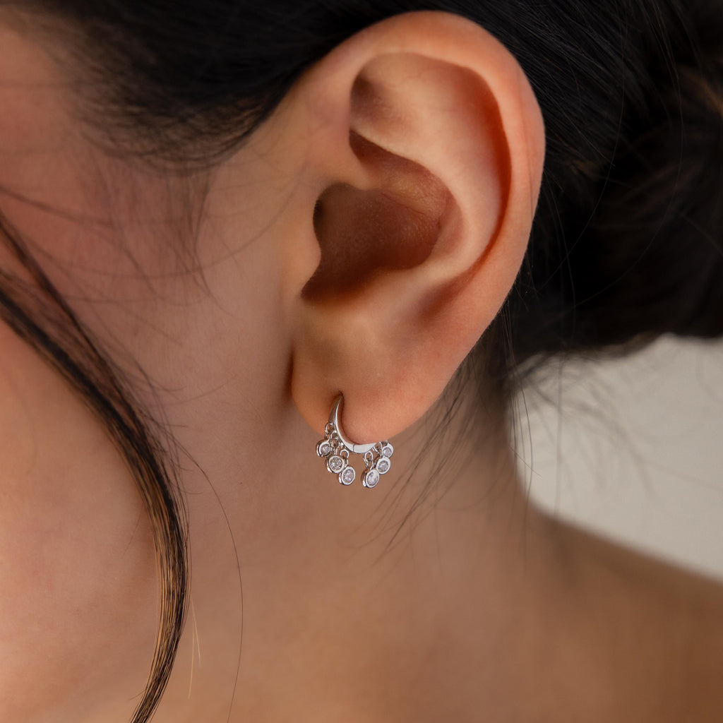 Close-up of a woman's ear wearing Chandelier Diamond Huggies, featuring delicate silver and sparkling crystal diamonds for a refined look.
