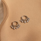 The Chandelier Diamond Huggies shimmer on a tan surface, showcasing timeless elegance and an art deco-inspired charm.