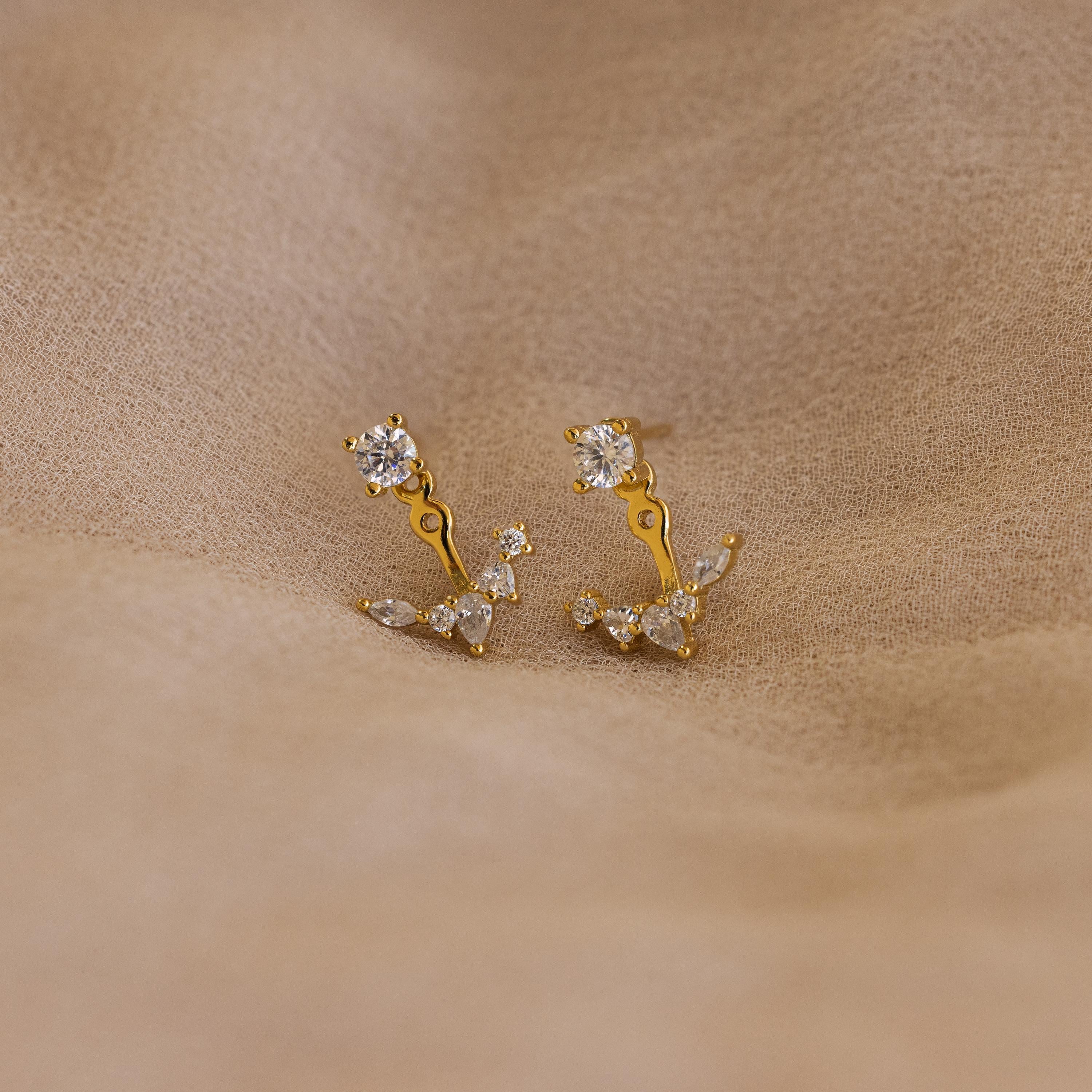 Diamond Cluster Ear Jackets featuring a delicate floral design, with gold and diamond studs, displayed on a beige fabric background.