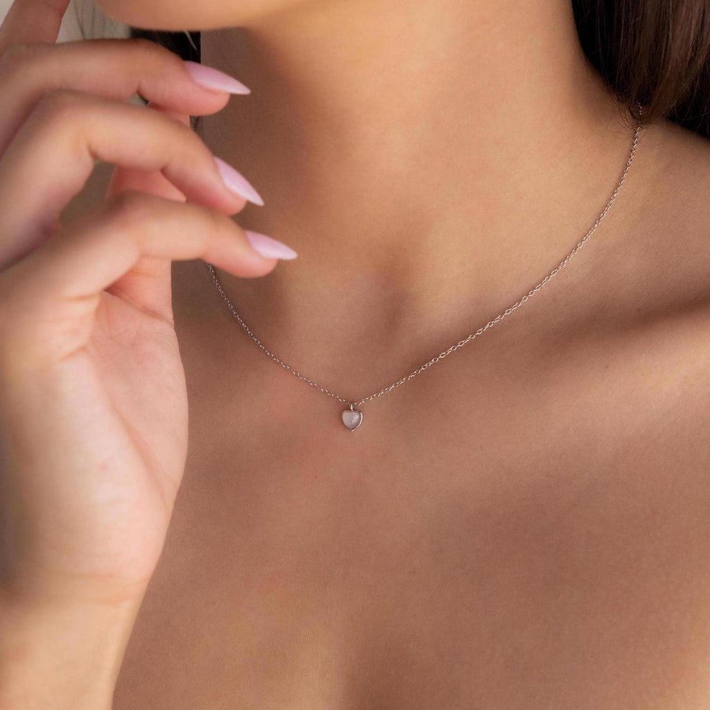 A woman showcases the Tiny Rose Quartz Heart Necklace, her manicured nails elegantly posed near her face.