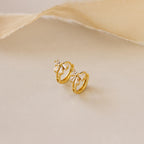 Close-up of Diamond Ribbon Bow Huggies in Gold set against a cream background.