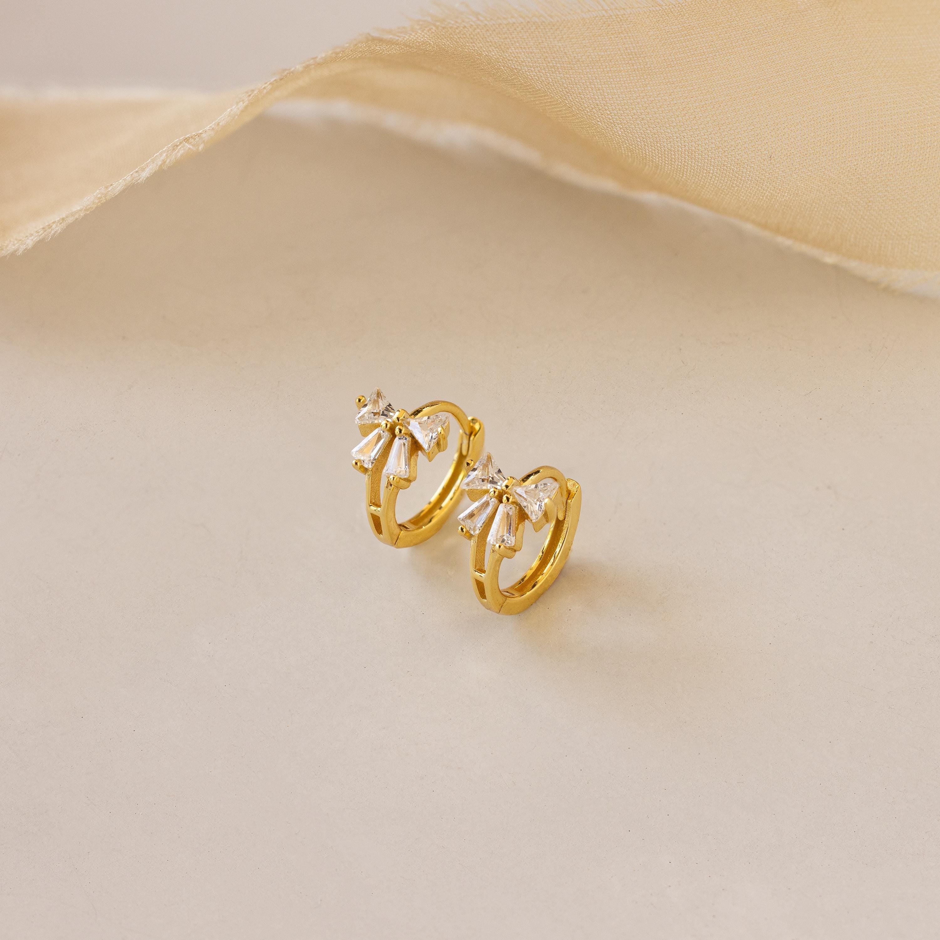 Close-up of Diamond Ribbon Bow Huggies in Gold set against a cream background.