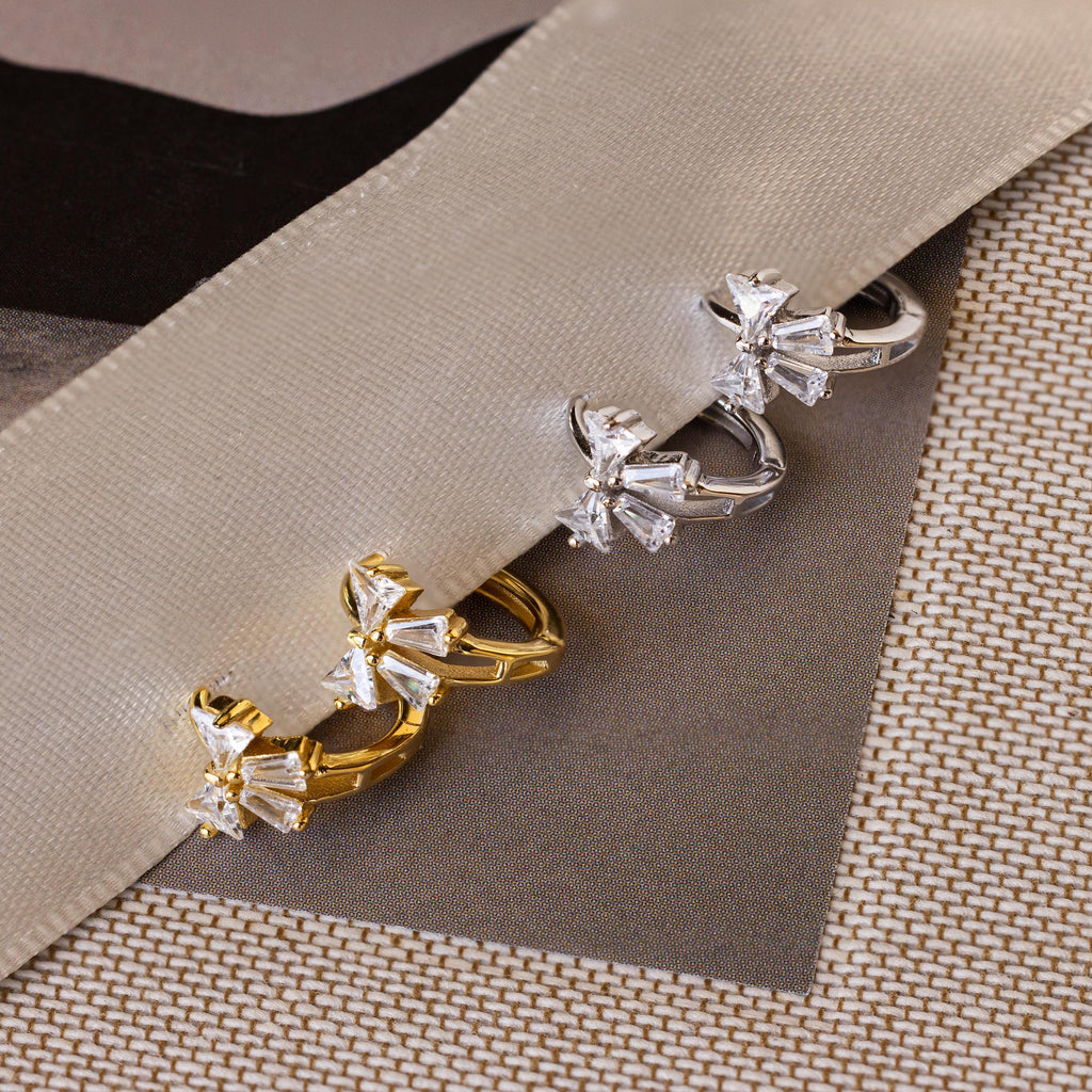 Close-up of Diamond Ribbon Bow Huggies in Gold & Silver laying on a gray ribbon.