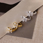 Close-up of Diamond Ribbon Bow Huggies in Gold & Silver laying on a gray ribbon.