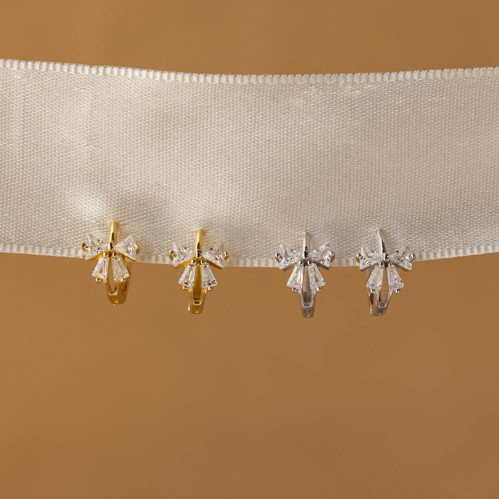 Close-up of Gold and Silver Diamond Ribbon Bow Huggies hanging from a white fabric.