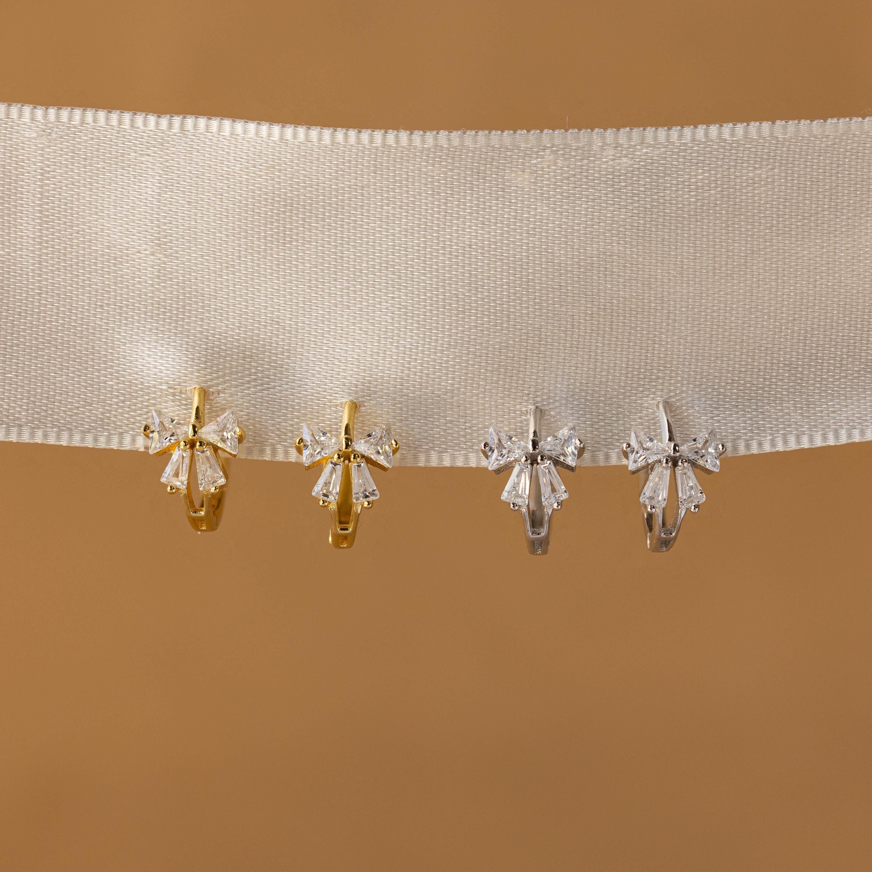 Close-up of Gold and Silver Diamond Ribbon Bow Huggies hanging from a white fabric.