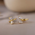 Diamond Bow Huggies featuring two clear, teardrop-shaped gems stacked vertically, displayed on a soft, neutral background.