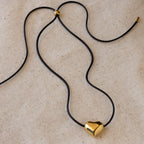 Chunky Puff Heart Necklace with a black cord and shiny gold heart pendant, displayed on beige fabric—perfect for those who love bold heart jewelry.