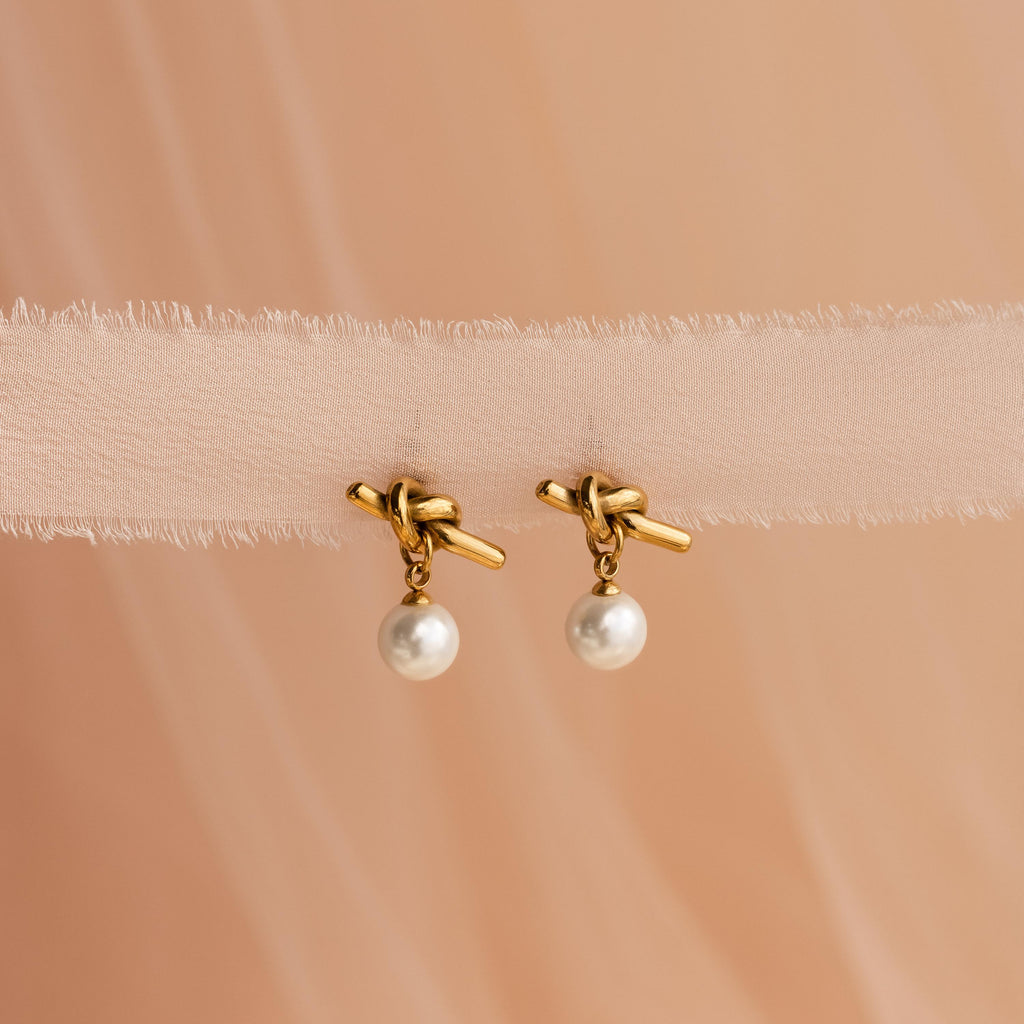 Love Knot Pearl Earrings featuring elegant pearl drops, beautifully displayed on soft beige fabric—a classic accessory for weddings.