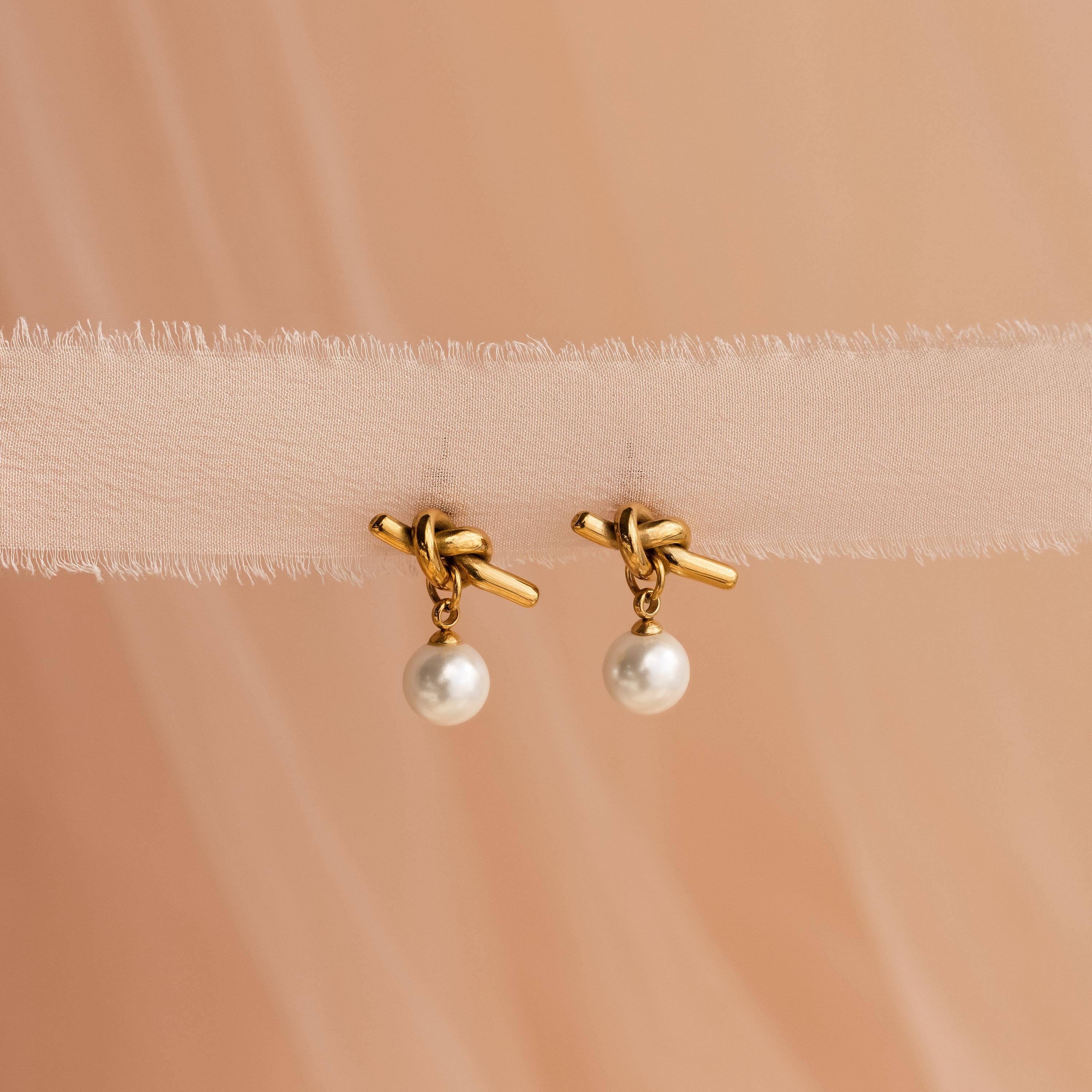 Love Knot Pearl Earrings featuring elegant pearl drops, beautifully displayed on soft beige fabric—a classic accessory for weddings.