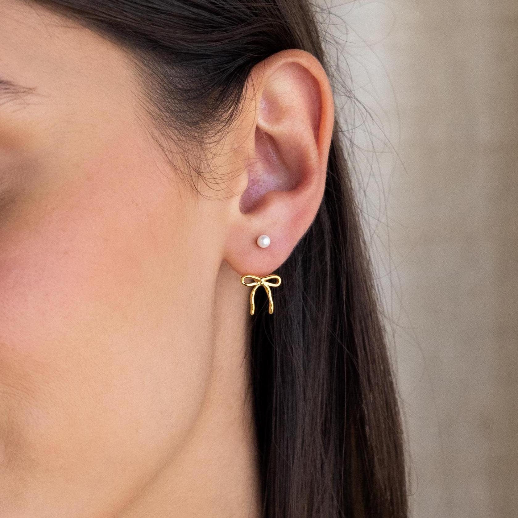 Close-up of an ear wearing the Pearl & Bow Ear Jackets, featuring a refined pearl stud and stylish gold bow detail on the earlobe.