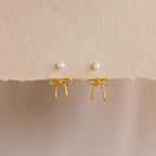 Two Pearl & Bow Ear Jackets, featuring gold bows and small pearl studs, are displayed on a textured beige background—perfect for adding elegance to your look.