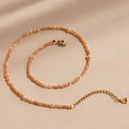 The Blush Pearl Beaded Necklace features pink freshwater pearls with a gold clasp and extender, elegantly displayed on a beige background.