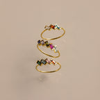 The Multiple Baguette Birthstone Ring is a gold spiral stackable ring with colorful rectangular gemstones, shown on a beige background.