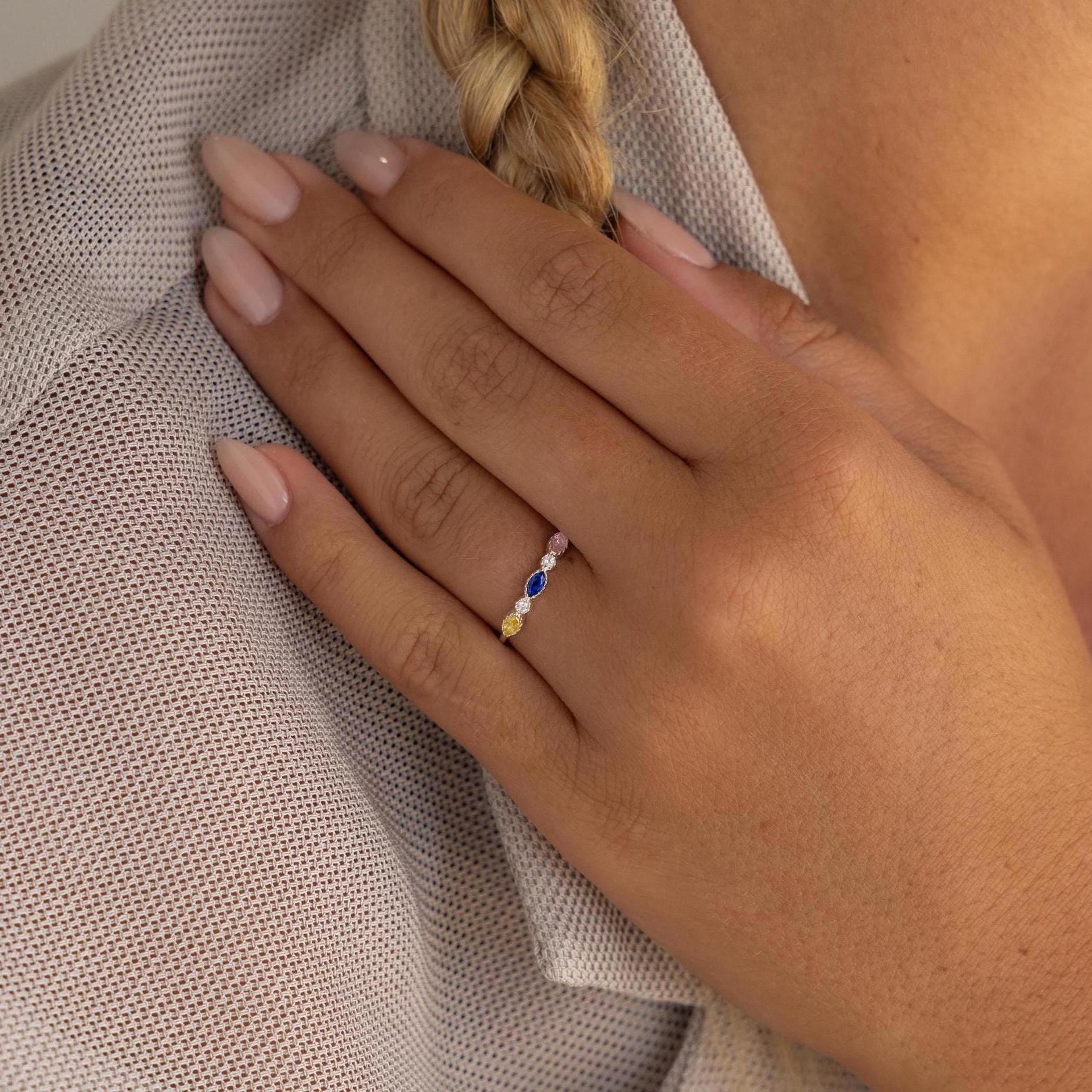 A hand with manicured nails wears the Cluster Marquise Birthstone Ring, featuring marquise-cut gemstones, gently resting on a shoulder in a mesh shirt.