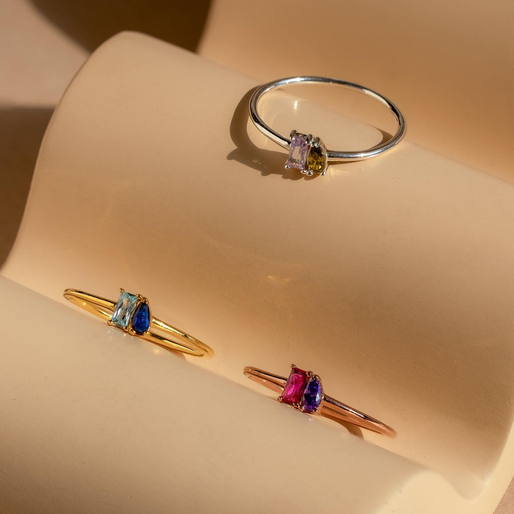 A set of customizable rings on a stand, featuring elegant birthstone styles such as the Tiny Toi et Moi Birthstone Ring.