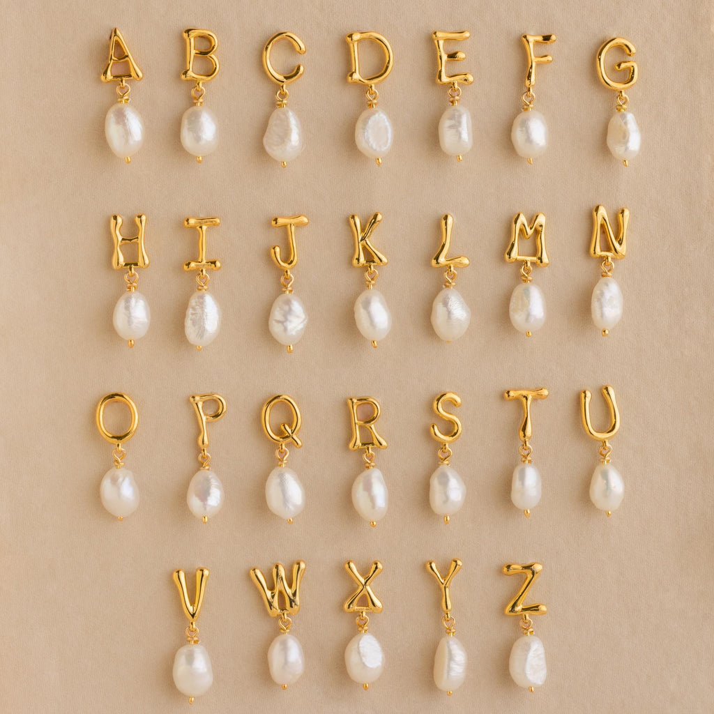 Initial Pearl Drop Studs featuring gold letter charms with dangling pearls, beautifully arranged on a beige background—ideal for creating personalized initial earrings or custom stud earrings.