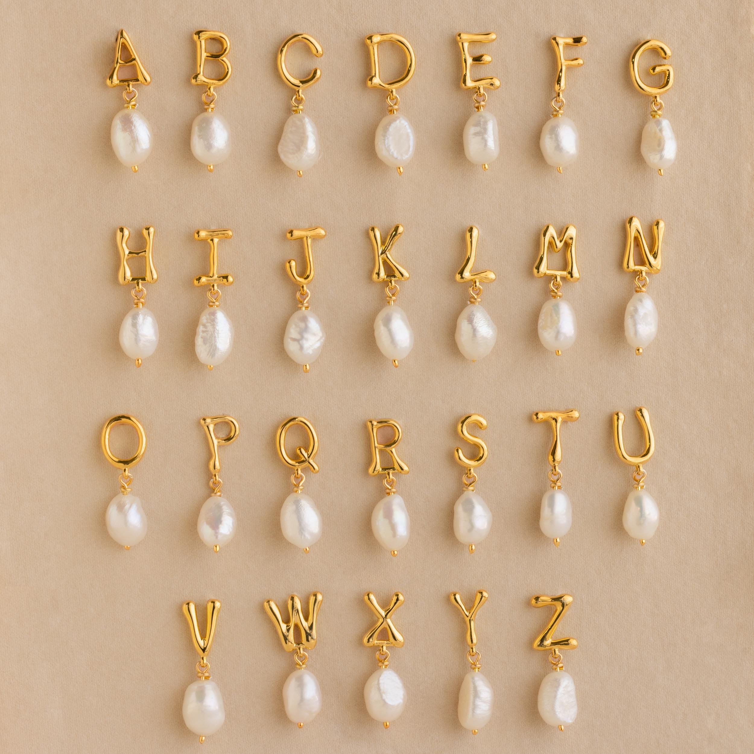 Initial Pearl Drop Studs featuring gold letter charms with dangling pearls, beautifully arranged on a beige background—ideal for creating personalized initial earrings or custom stud earrings.