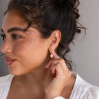A woman with her hand on her ear, showcasing elegant Initial Pearl Drop Studs that add a touch of unique charm to her look.