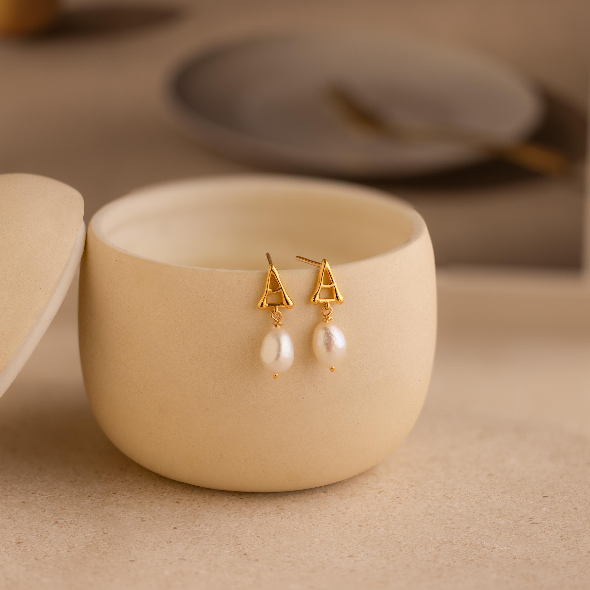 A pair of Initial Pearl Drop Studs in a container.