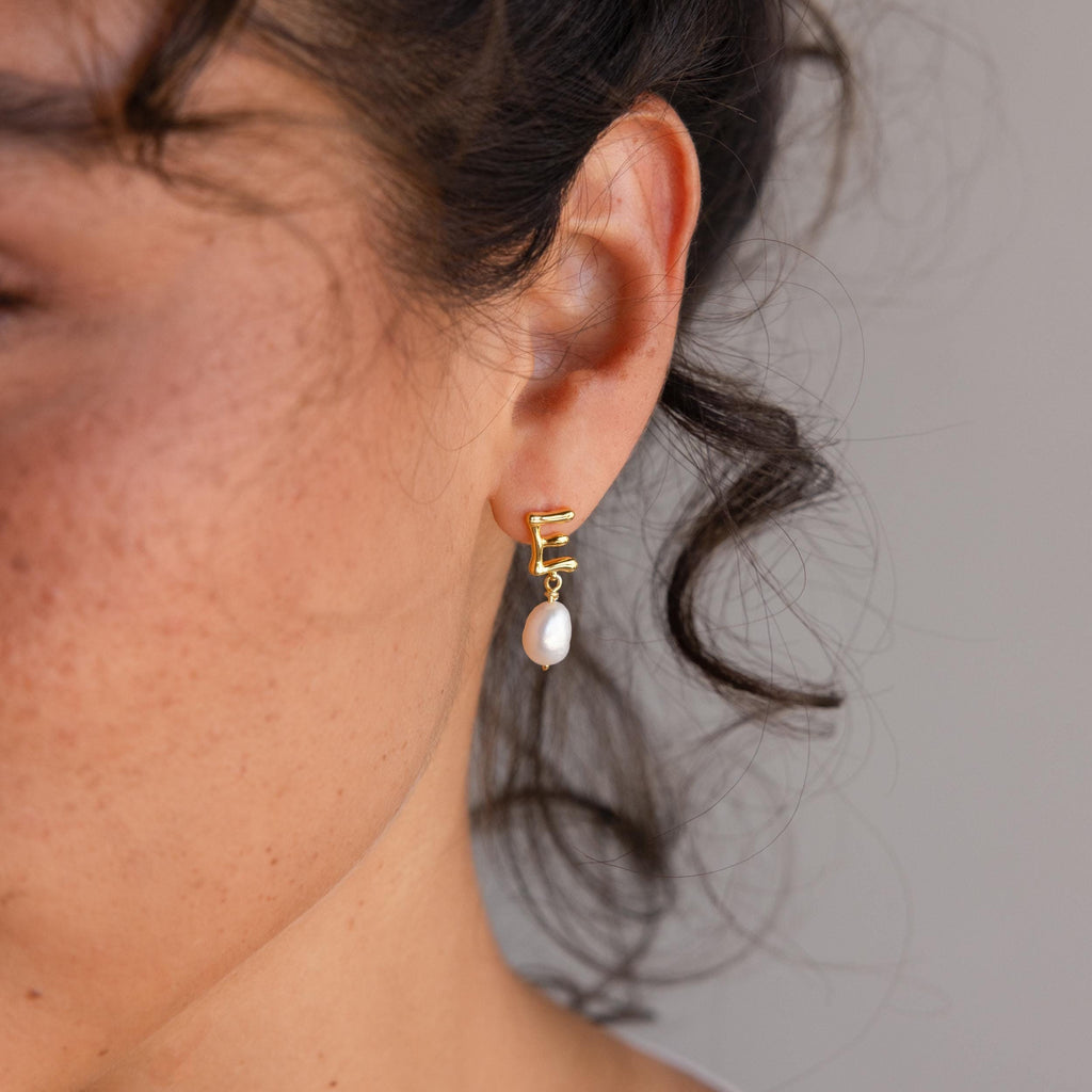 A close-up of a woman's ear adorned with elegant Initial Pearl Drop Studs.