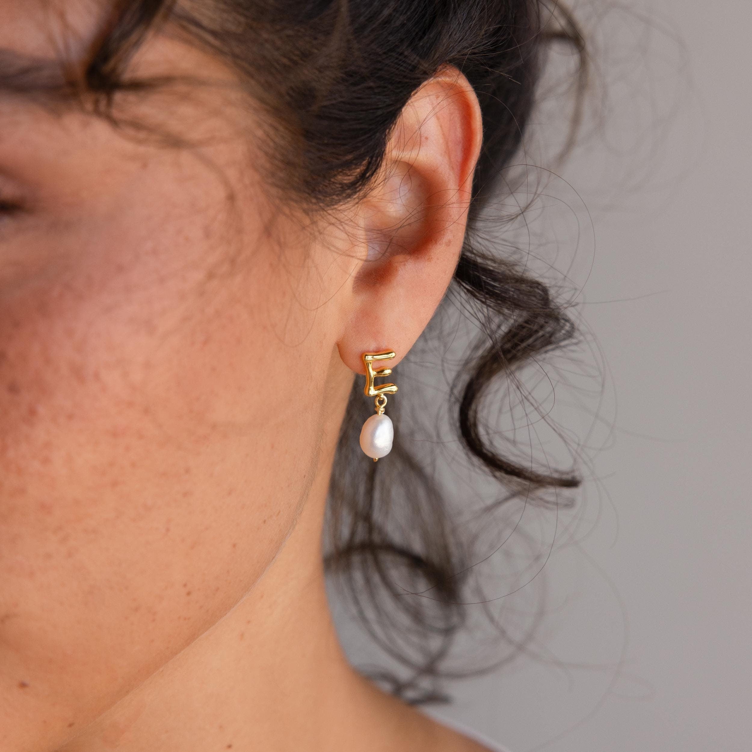 A close-up of a woman's ear adorned with elegant Initial Pearl Drop Studs.