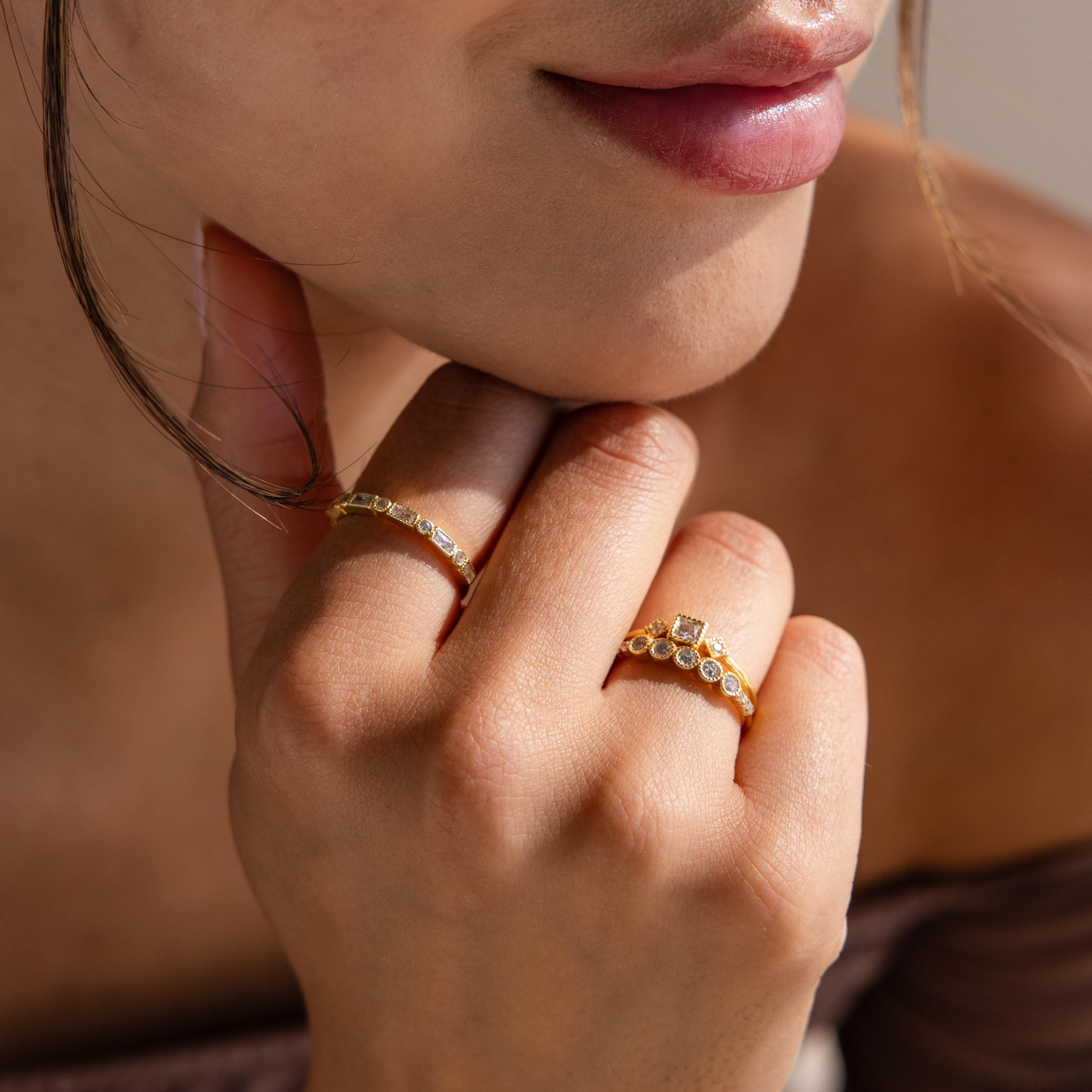 Close-up of a model wearing a gold Art Deco diamond ring set on two fingers, with her hand gently resting on her chin.