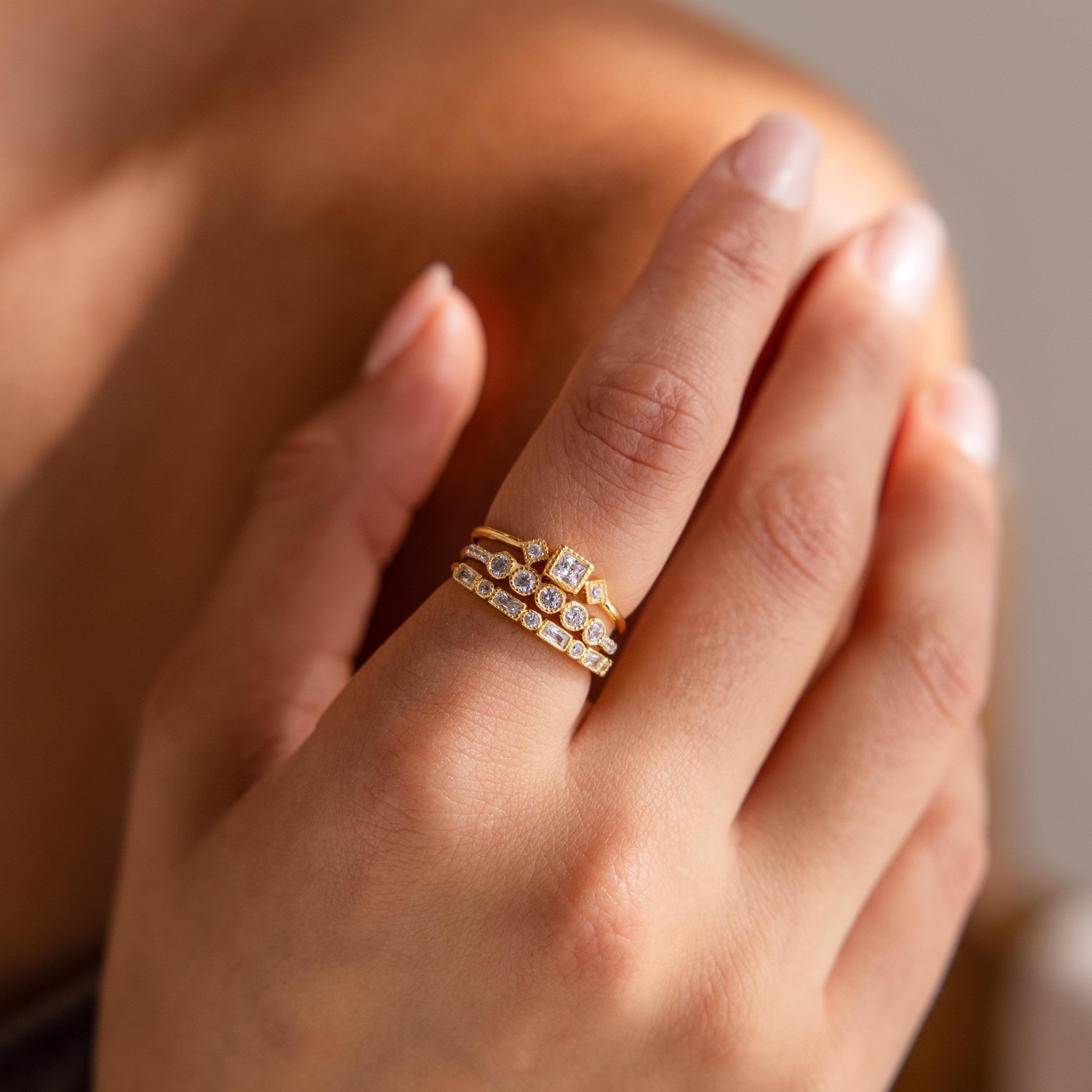 A hand with manicured nails wears stacked gold rings, spotlighting the Art Deco Diamond Ring Set for a touch of vintage glamour on the ring finger.