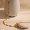 The Pave Link Chain Necklace with rectangular links is displayed draped over a smooth white vase and a stone on a beige surface.