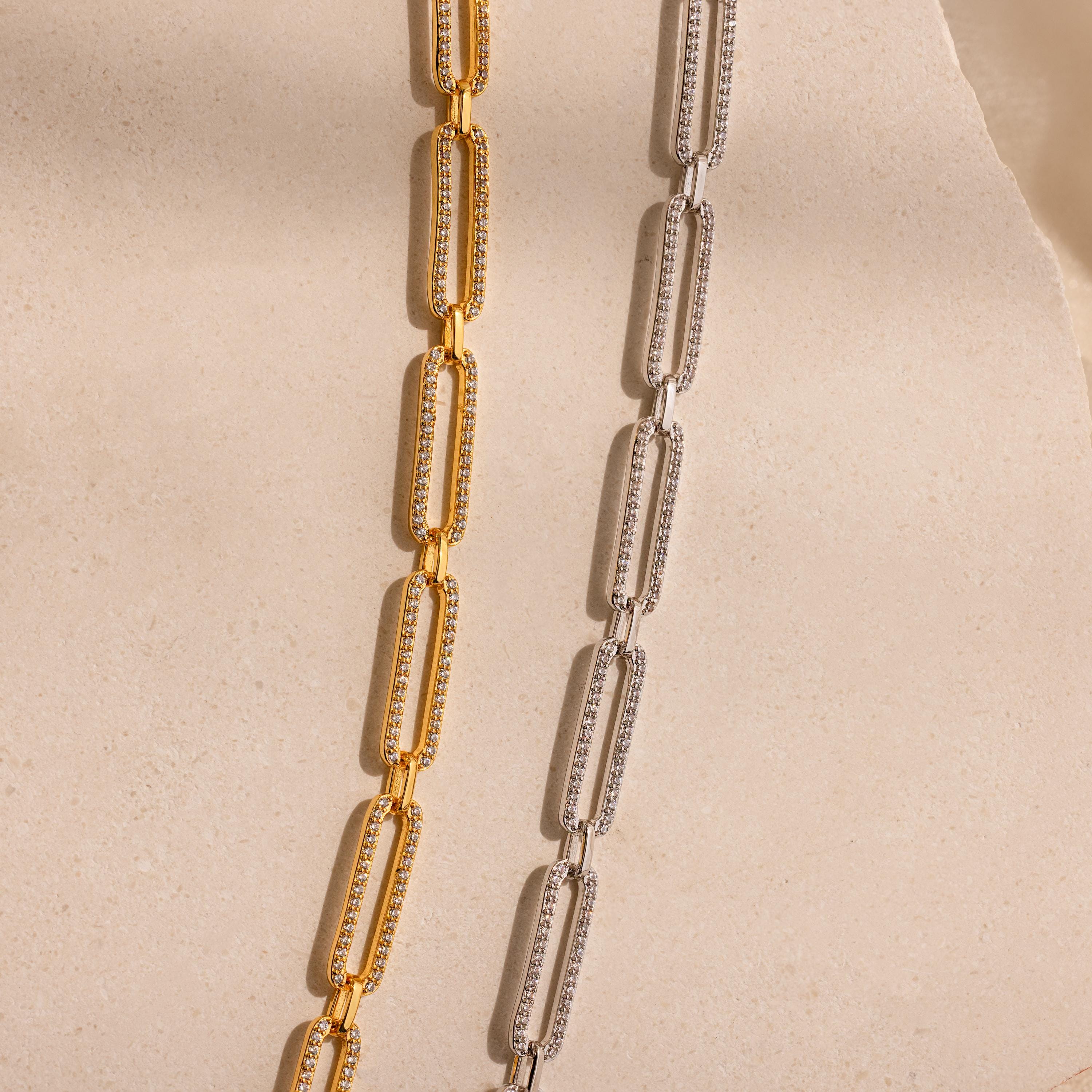 The Pave Link Chain Necklace is displayed on a textured beige surface with soft lighting, showcasing its rectangular gold and silver links.