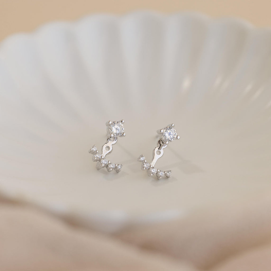 Round Diamond Ear Jackets in Sterling Silver, featuring arc design gemstone accents, reminiscent of elegant diamond stud earrings, displayed on a white shell-shaped dish.