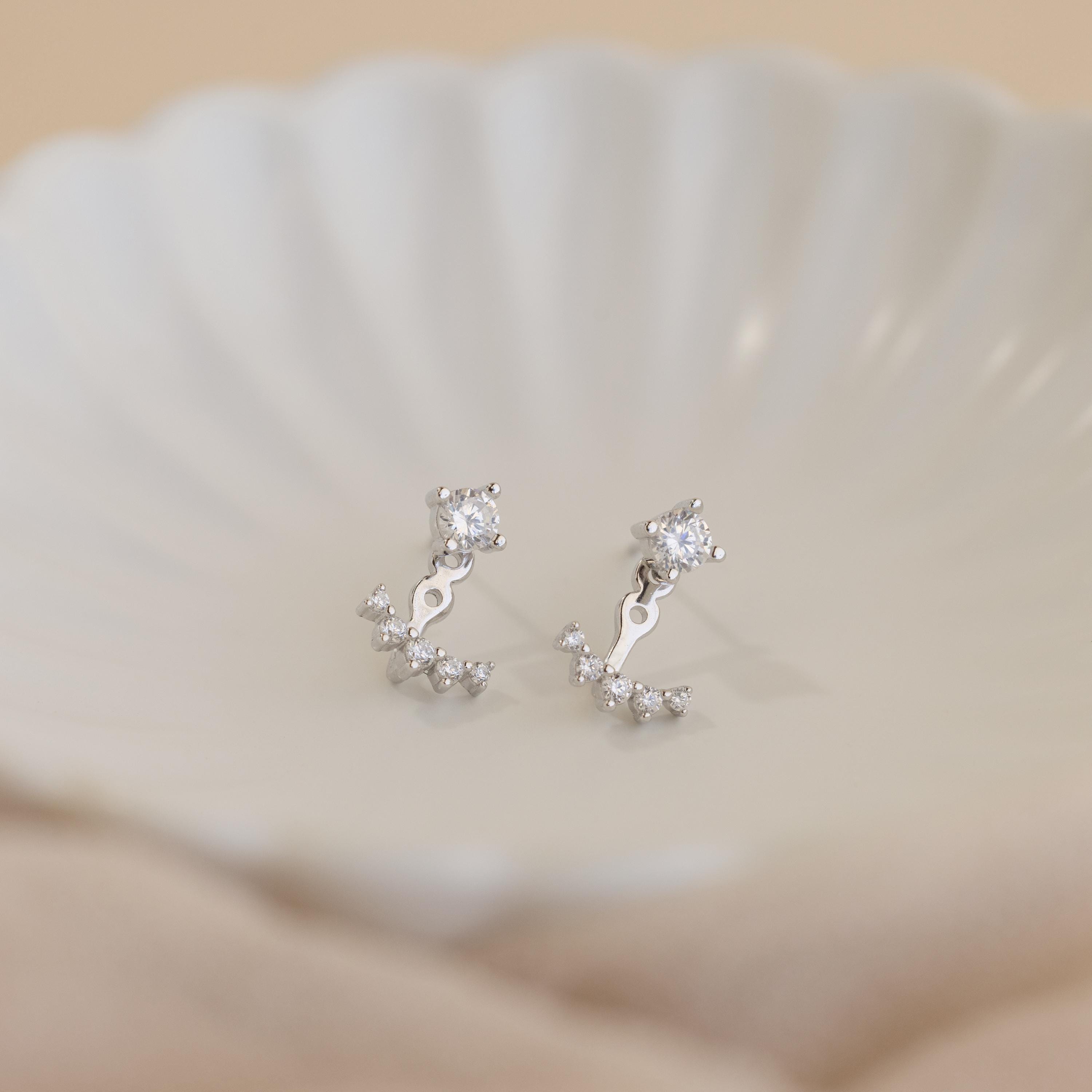Round Diamond Ear Jackets in Sterling Silver, featuring arc design gemstone accents, reminiscent of elegant diamond stud earrings, displayed on a white shell-shaped dish.