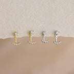 A pair of Round Diamond Ear Jackets in 18K Gold, paired with crystal-studded studs and displayed on a textured surface.