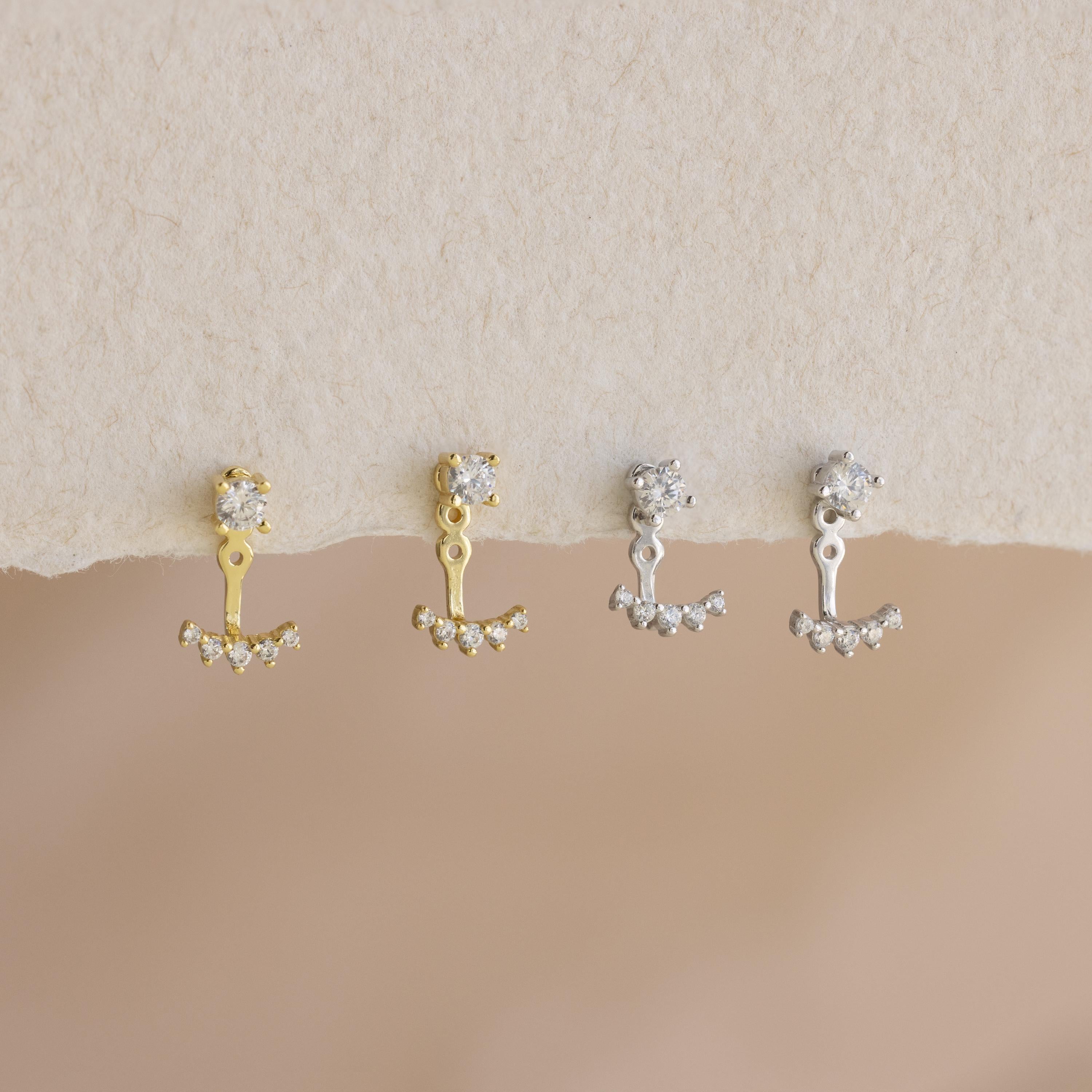 A pair of Round Diamond Ear Jackets in 18K Gold, paired with crystal-studded studs and displayed on a textured surface.