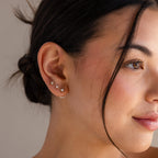A close-up of a woman's face, her ears adorned with dainty studs and Round Diamond Ear Jackets in 18K Gold that catch the light beautifully.