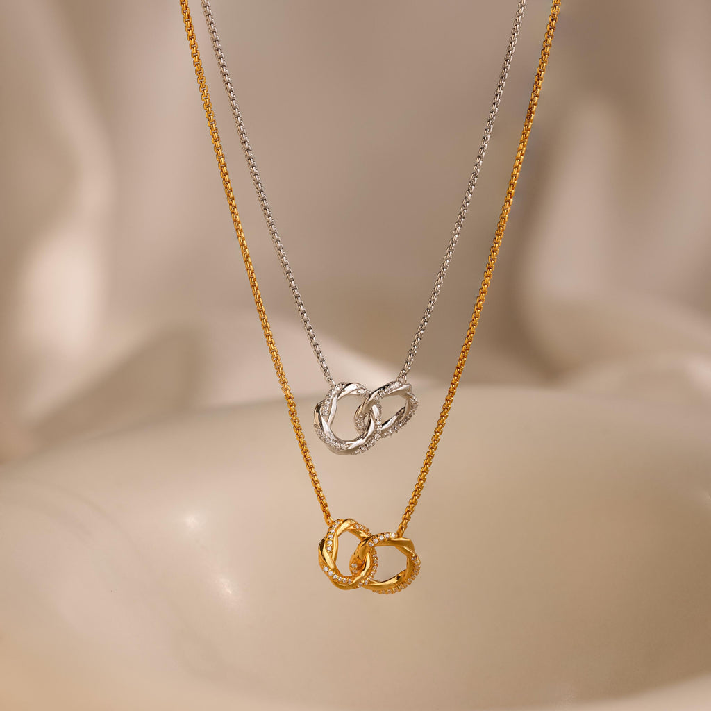The Interlocking Pave Charm Necklace, featuring gold and silver mother-daughter circle pendants, is displayed against a soft, neutral background.