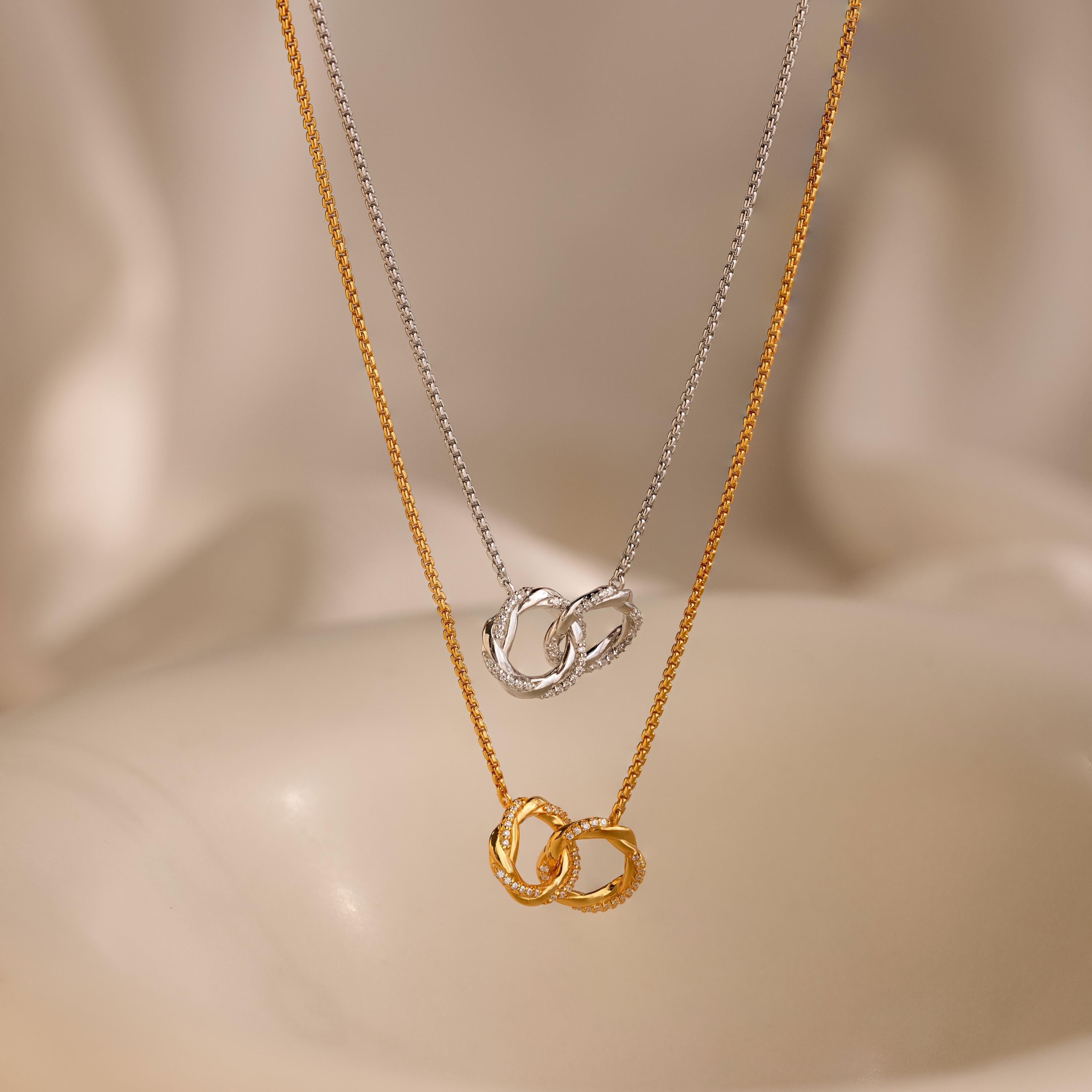 The Interlocking Pave Charm Necklace, featuring gold and silver mother-daughter circle pendants, is displayed against a soft, neutral background.