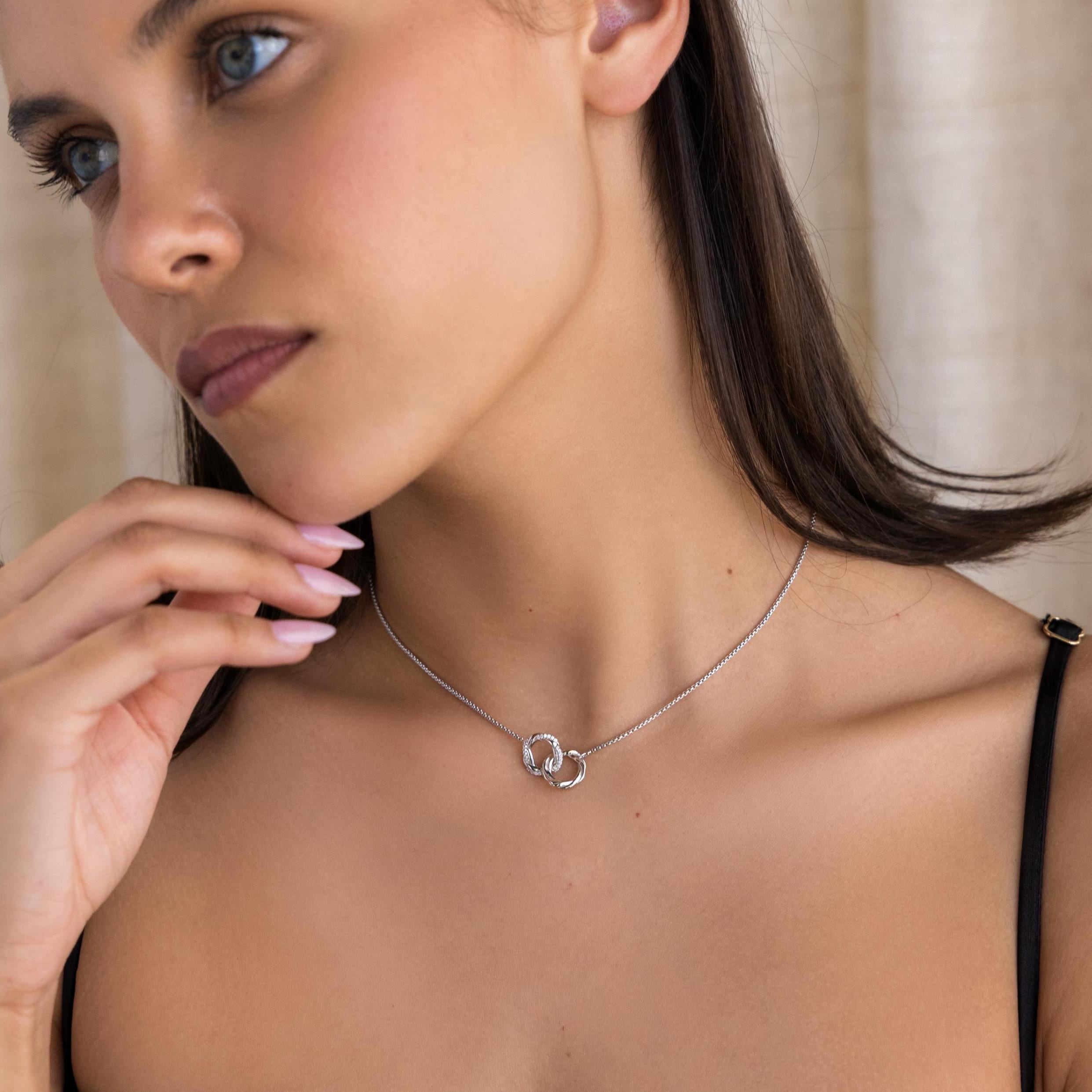 A woman in a black strap top, wearing the Interlocking Pave Charm Necklace with silver rings, gazes to the side.