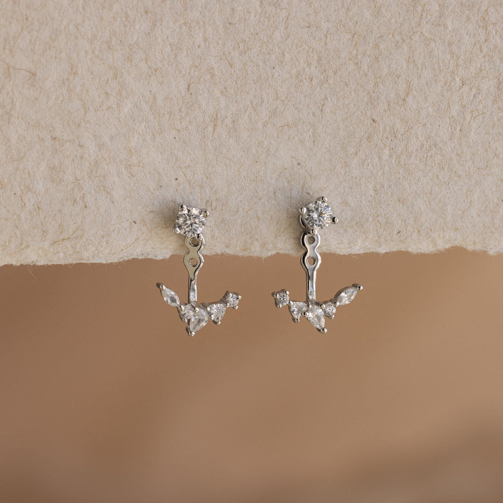 The Diamond Cluster Ear Jackets feature a front back design with small, sparkling crystals set in silver, displayed against a textured beige background.