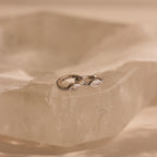 Two elegant Marquise Pave Huggies with bezeled marquise gemstones rest on a translucent, faceted crystal surface.