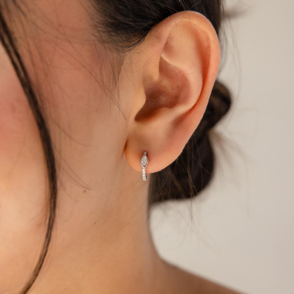 A close-up of a woman's ear adorned with Marquise Pave Huggies featuring a bezeled marquise gemstone in an art deco-inspired design.