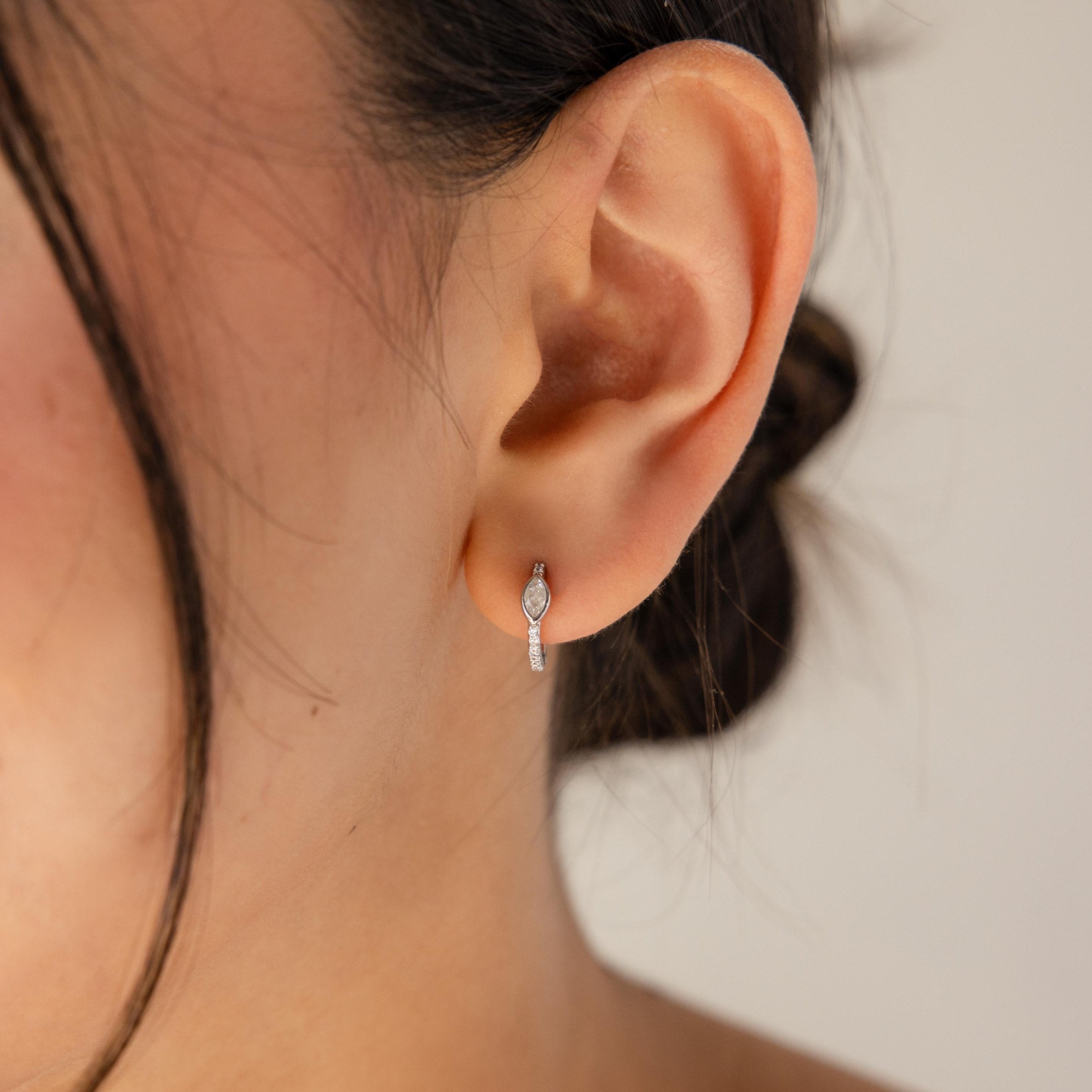 A close-up of a woman's ear adorned with Marquise Pave Huggies featuring a bezeled marquise gemstone in an art deco-inspired design.