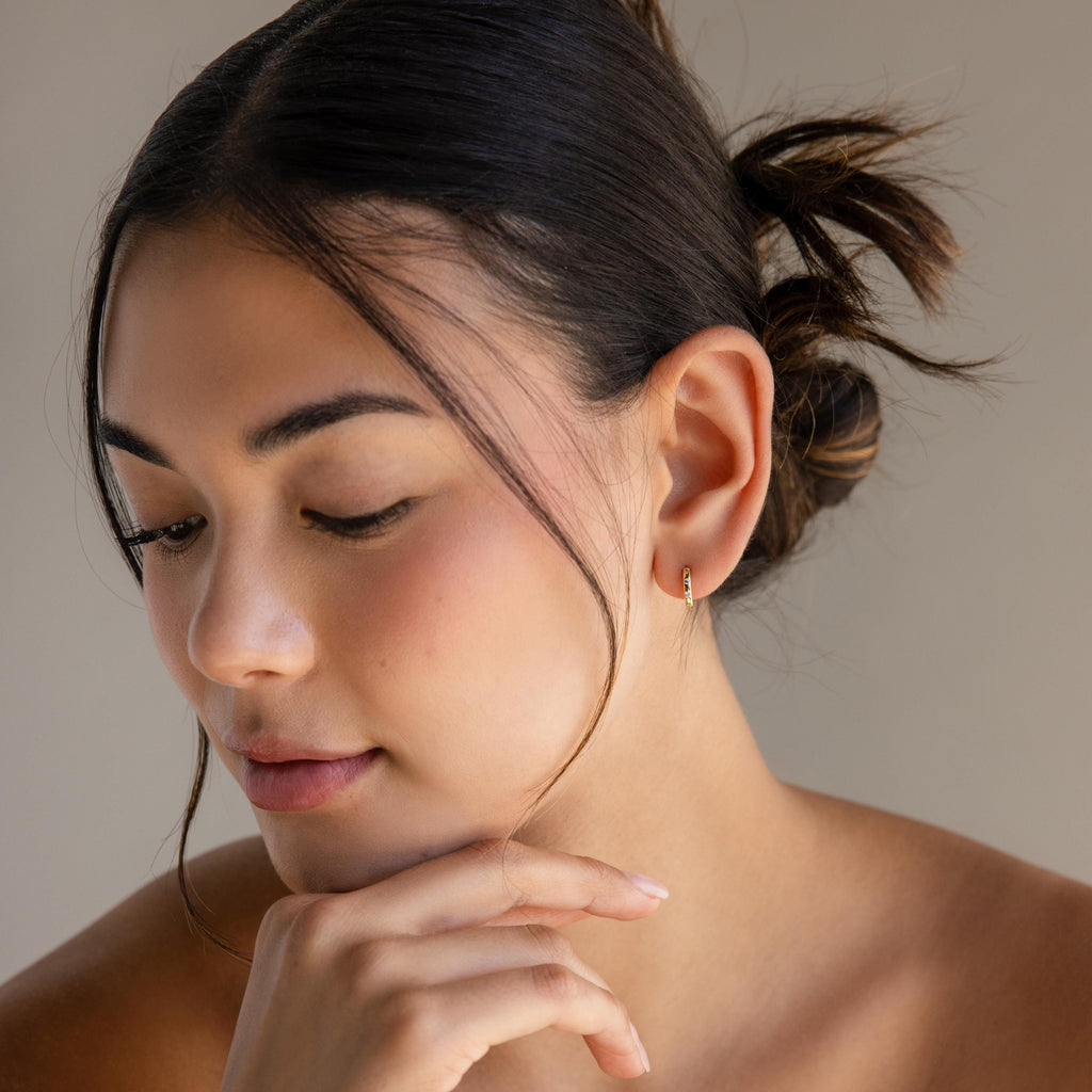 A woman with her hand on her chin elegantly showcases the Mini Diamond Sprinkle Huggies.