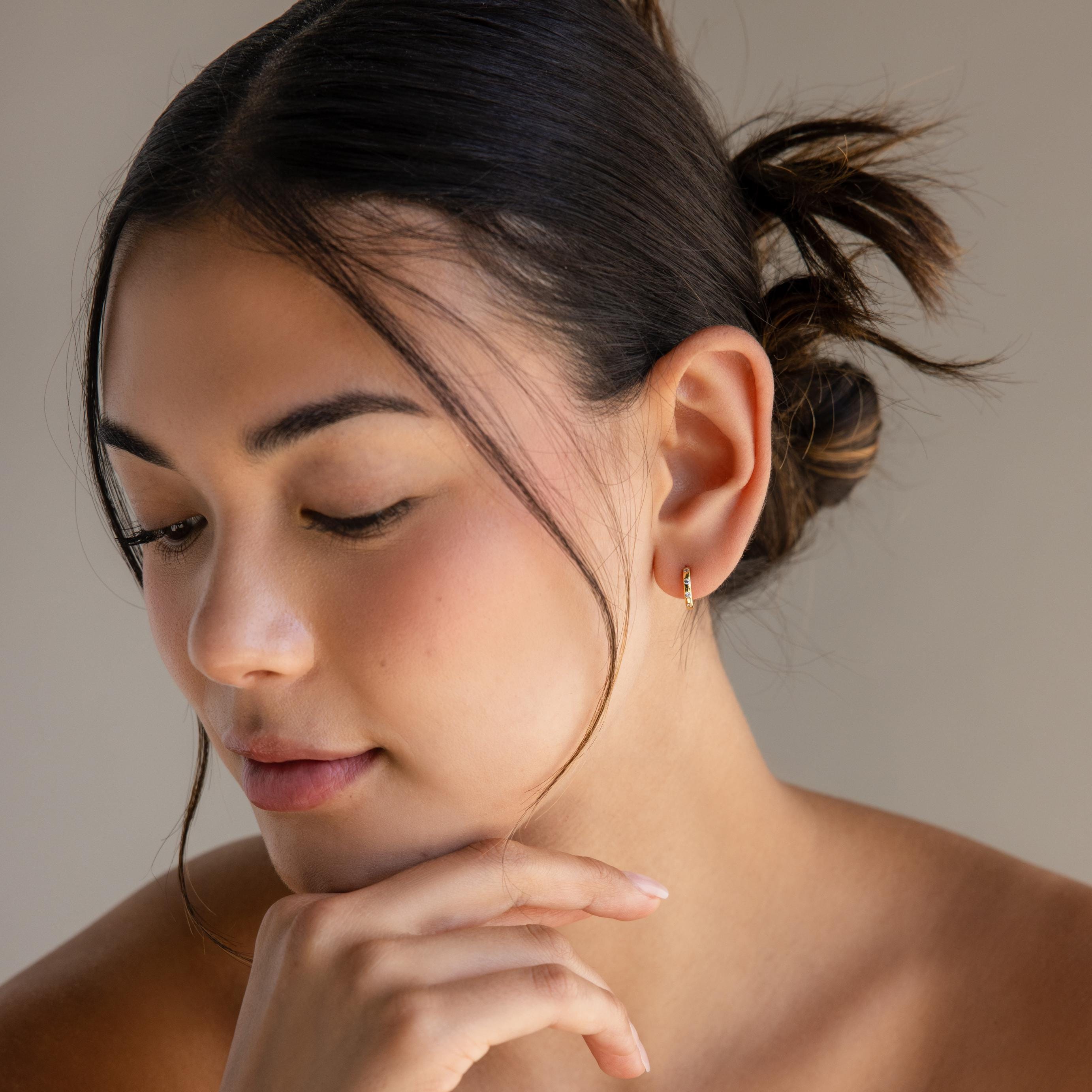 A woman with her hand on her chin elegantly showcases the Mini Diamond Sprinkle Huggies.