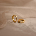 Two Mini Diamond Sprinkle Huggies, crafted in gold and accented with small diamonds, are displayed on a soft beige fabric background.