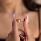 A woman holds the Trio Diamond Stacking Ring Set—featuring elegant gold and diamond rings—between her fingers, against a blurred background.