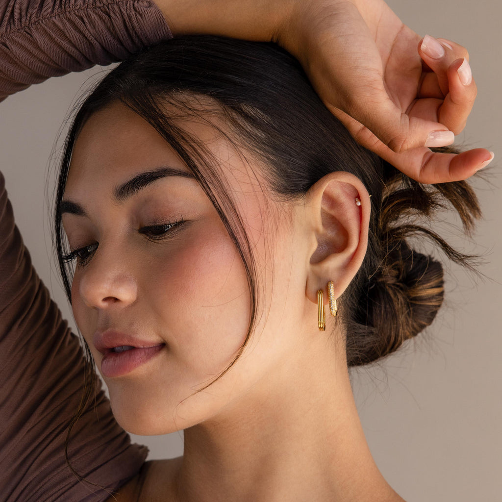 Woman with dark hair in a bun wears Chunky Pave Link Earrings, looking down with one arm raised above her head.
